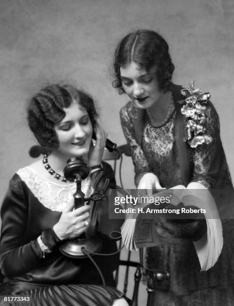 two women 1 is on the phone the other is showing her a number in the phone directory both are wearing dressey dresses smiling white & black lace. - candlestick phone - fotografias e filmes do acervo