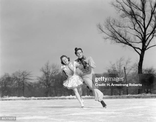 man woman couple pair figure skating on ice rink smiling costumes arm in arm leaning precision glide dance. - figure skating couple stock pictures, royalty-free photos & images