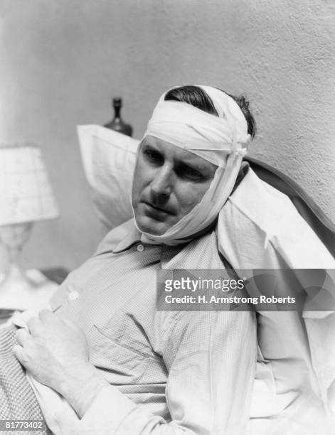 man in bed with bandage around head and chin, looks in pain from mumps, toothache or injury. - 1940s bedroom stock pictures, royalty-free photos & images