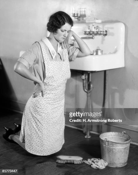 woman on her knees, with hand on hip and elbow on the sink and a frown on her face. she is wearing an apron over her dress, with scrub brush and pail on the floor, with rag.  (photo by h. armstrong roberts/retrofile/getty imag - bored housewife 個照片及圖片�檔