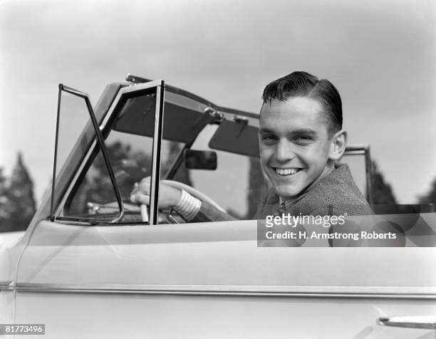 young man smiling at camera, sitting at steering wheel of convertible car. - 1940 18-21 stock pictures, royalty-free photos & images