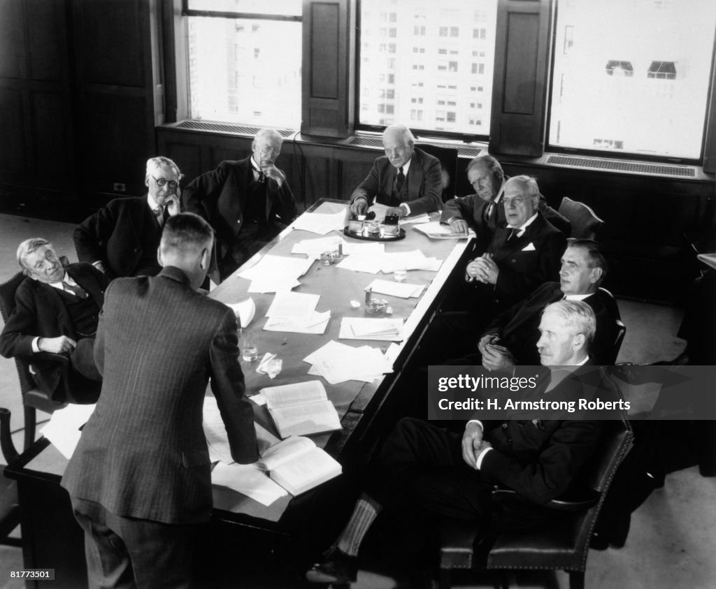 Elderly Businessmen At Conference Table With 1 Man Standing & Talking