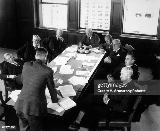 elderly businessmen at conference table with 1 man standing & talking  - 40's rumpled business man stockfoto's en -beelden