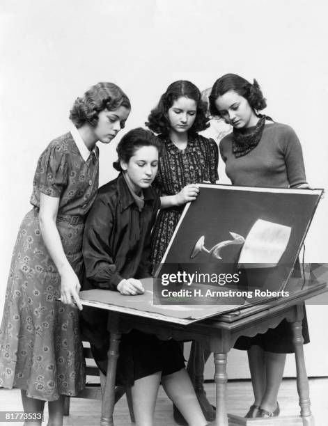 3 young women observe a fourth draw artwork in portfolio. - group h foto e immagini stock