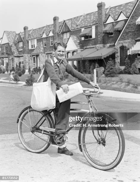 paperboy on bicycle in suburban neighborhood, with sack over shoulder and folded newspaper in hand. (photo by h. armstrong roberts/retrofile/getty images) - zeitungsausträger stock-fotos und bilder