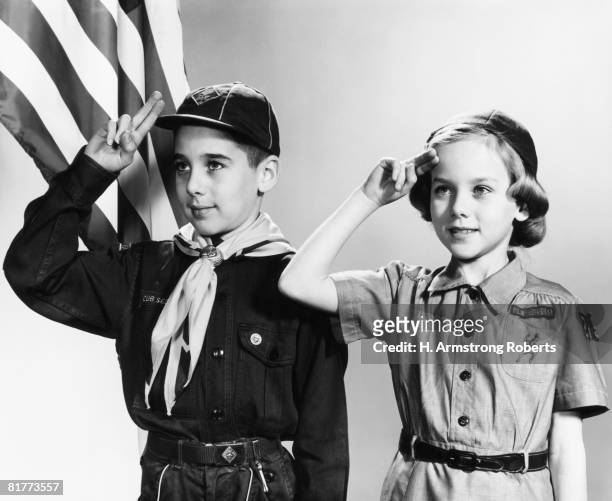 boy and girl scouts saluting, american flag in background. - girl scout stock-fotos und bilder