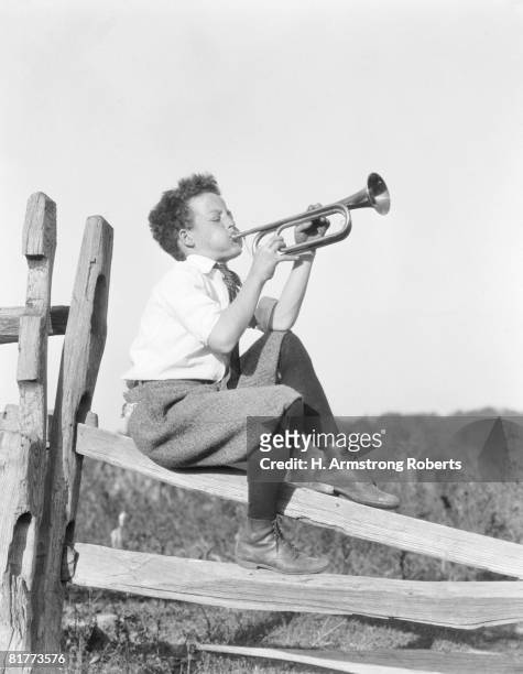boy sitting on fence, playing musical instrument. - 1930 stock pictures, royalty-free photos & images