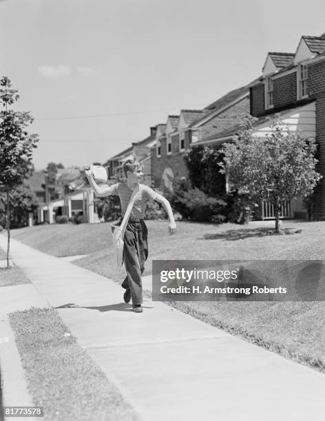 paperboy walking along suburban street, delivering newspapers. - zeitungsausträger stock-fotos und bilder