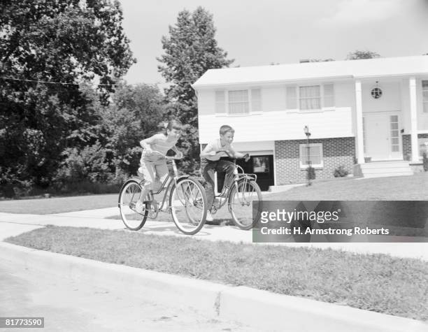 boy and girl racing along suburban street on bicycles. - retro boy stock-fotos und bilder