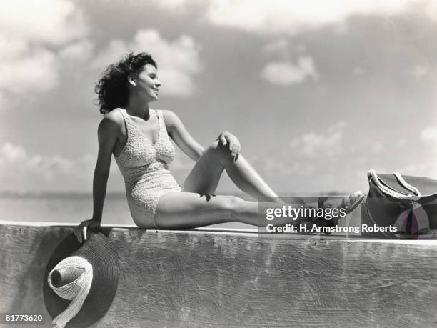 young woman wearing knitted swimsuit, posing on wall by ocean. (photo by h. armstrong roberts/retrofile/getty images) - monocromo vestuário - fotografias e filmes do acervo