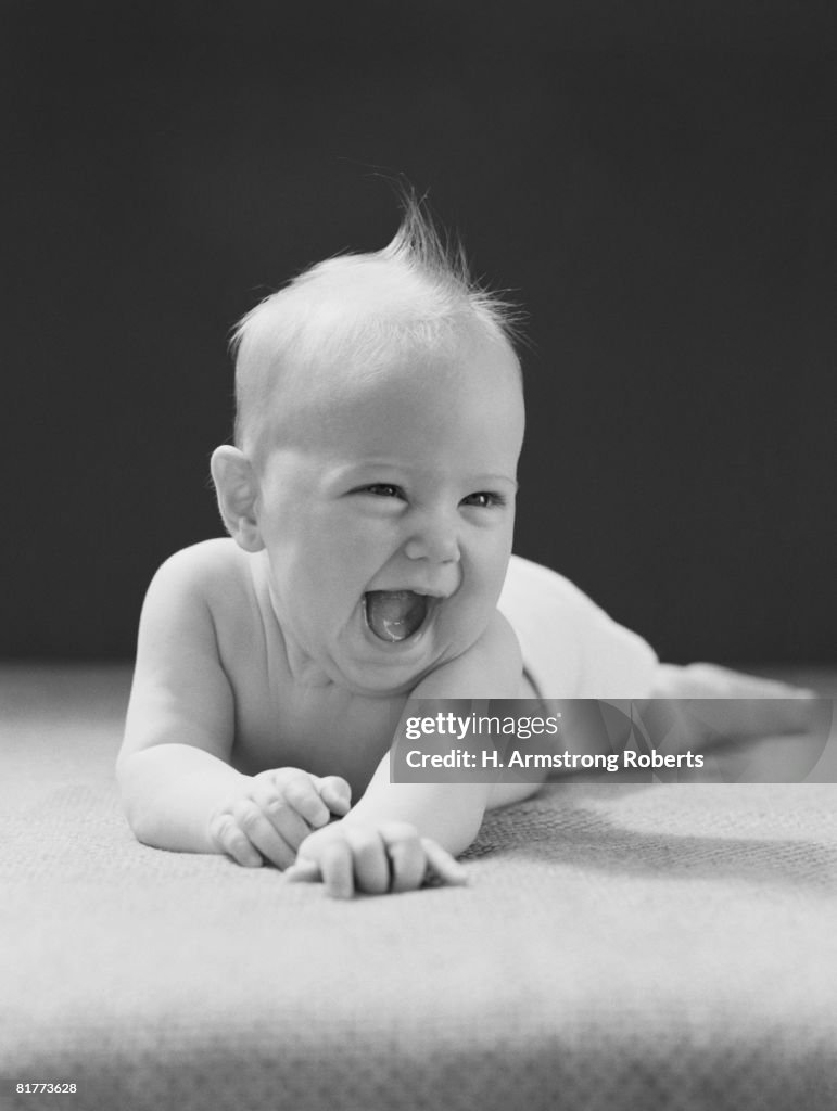 Five month old baby lying on stomach, arms outstretched, laughing.