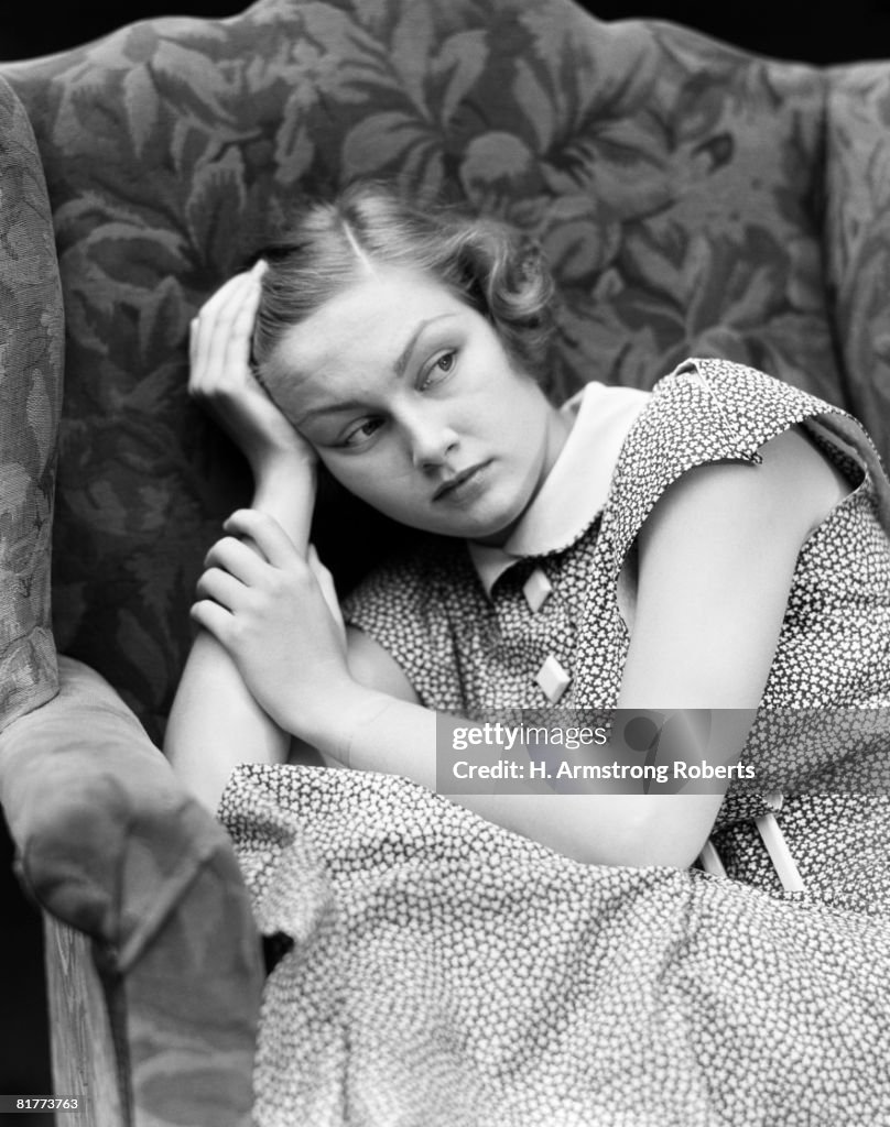 Worried woman sitting in chair with hand to head.