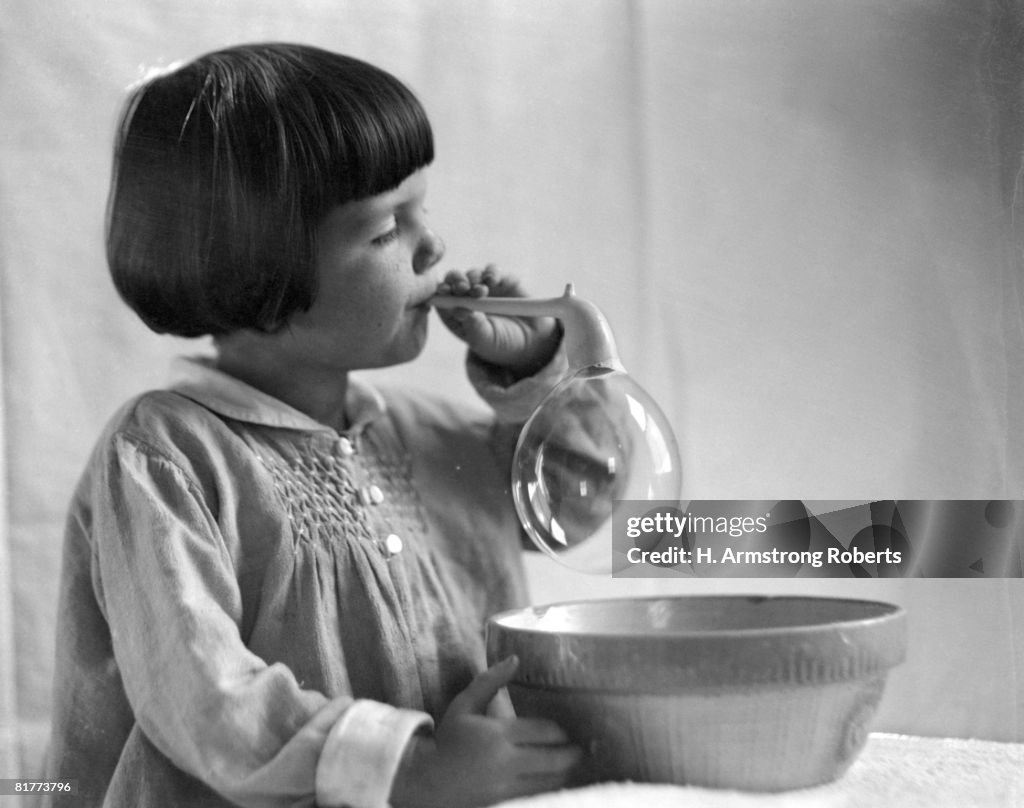 Girl with bobbed hair, blowing bubbles.