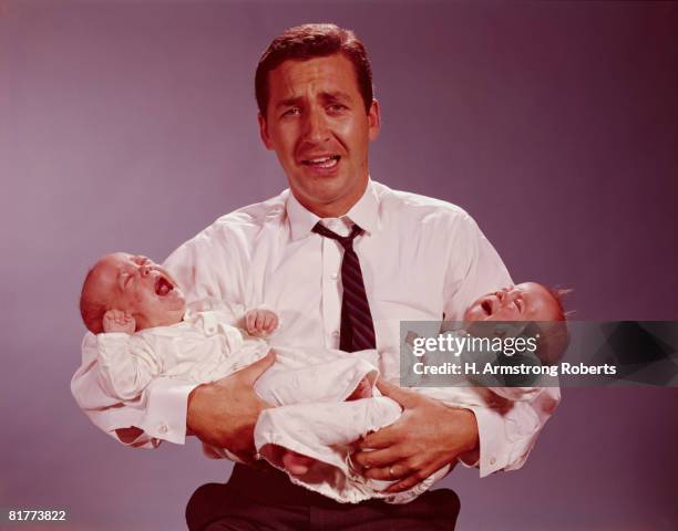 distressed looking father holding crying twin babies in his arms. (photo by h. armstrong roberts/retrofile/getty images) - 1950s father stock pictures, royalty-free photos & images