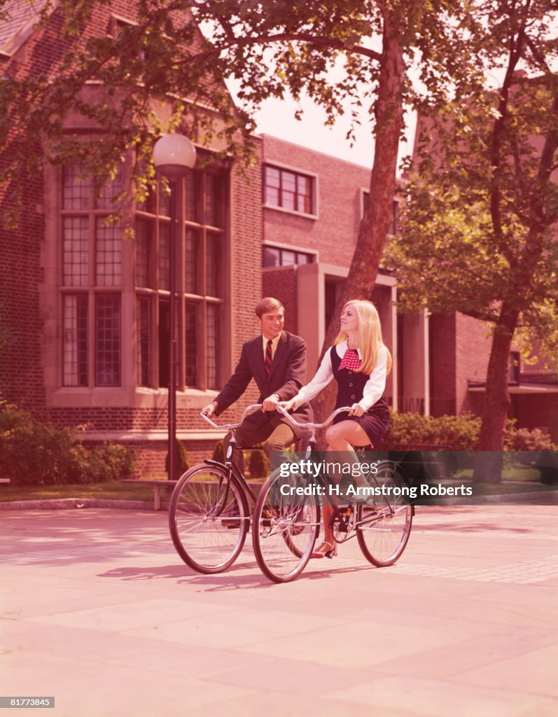 Teenage couple riding bicycles past high school buildings. (Photo by H. Armstrong Roberts/Retrofile/Getty Images)
