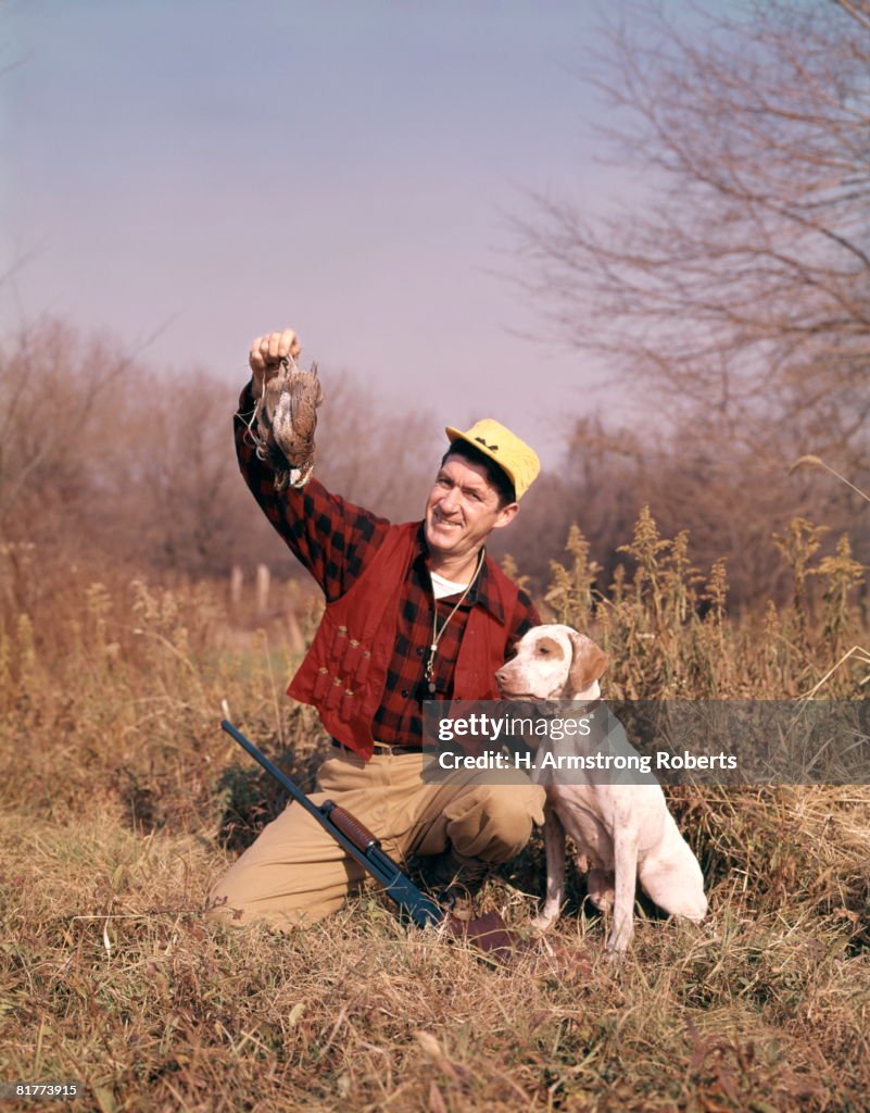 Hunter beside dog holding catch.