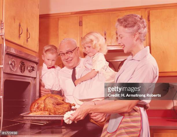 grandfather holding grandchildren and looking, grandmother removing roast turkey from oven. (photo by h. armstrong roberts/retrofile/getty images) - retro wife stock pictures, royalty-free photos & images