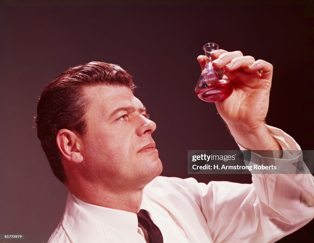 Scientific technician looking at coloured liquid in beaker. (Photo by H. Armstrong Roberts/Retrofile/Getty Images)