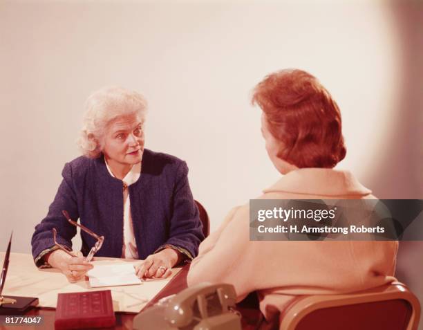 two businesswomen seated at desk, talking. (photo by h. armstrong roberts/retrofile/getty images) - 1960 stockfoto's en -beelden