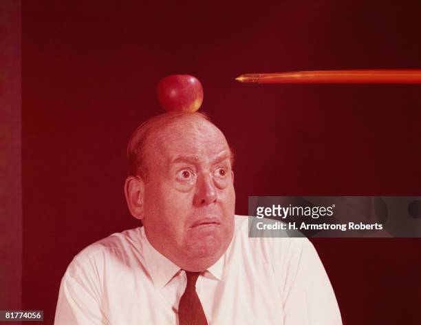 anxious man looking at arrow directed at apple on top of his head. (photo by h. armstrong roberts/retrofile/getty images) - apple arrow stock-fotos und bilder
