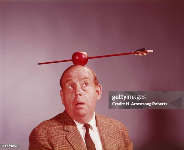 anxious looking man with apple pierced by arrow balanced on his head. (photo by h. armstrong roberts/retrofile/getty images) - apple arrow stock-fotos und bilder