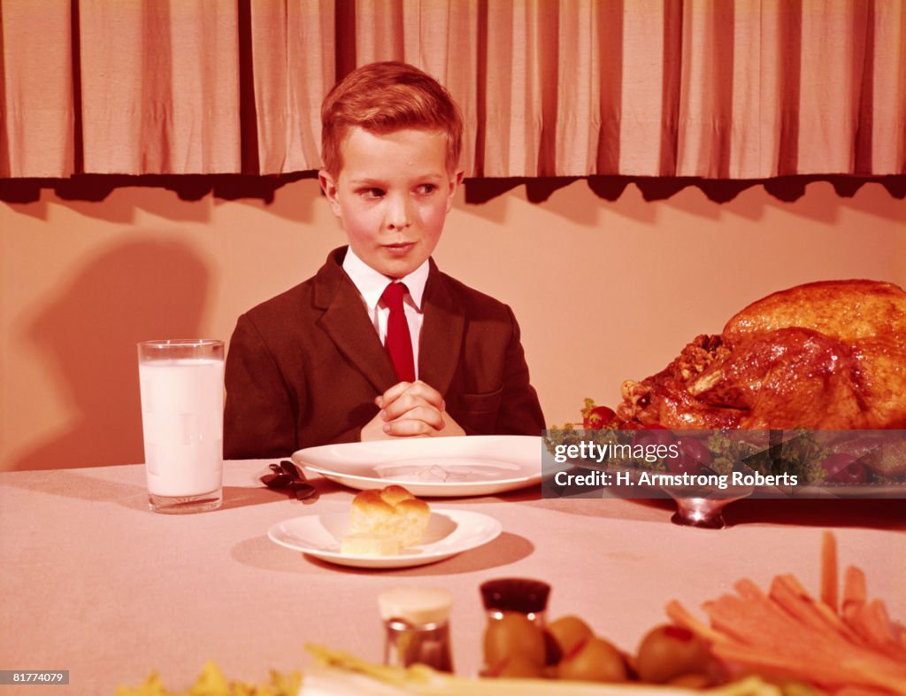 Boy sitting  at table with hands folded for grace prayer, looking at roast turkey. (Photo by H. Armstrong Roberts/Retrofile/Getty Images)