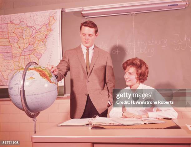 two male students standing by world globe, girl seated at desk in classroom. (photo by h. armstrong roberts/retrofile/getty images) - 1960 個照片及圖片檔