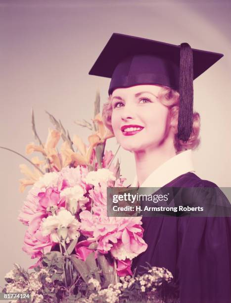 young woman wearing graduation robes and mortarboard, holding bouquet of flowers. (photo by h. armstrong roberts/retrofile/getty images) - headware stock pictures, royalty-free photos & images