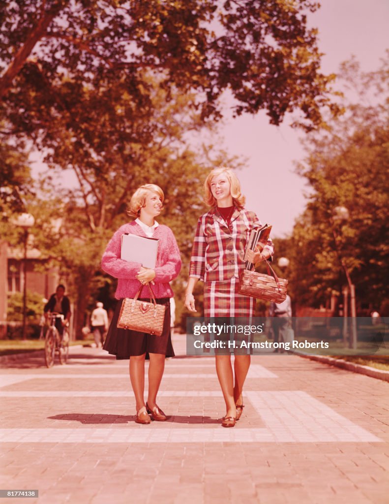 Two blonde female students walking on campus, carrying straw purses and books. (Photo by H. Armstrong Roberts/Retrofile/Getty Images)