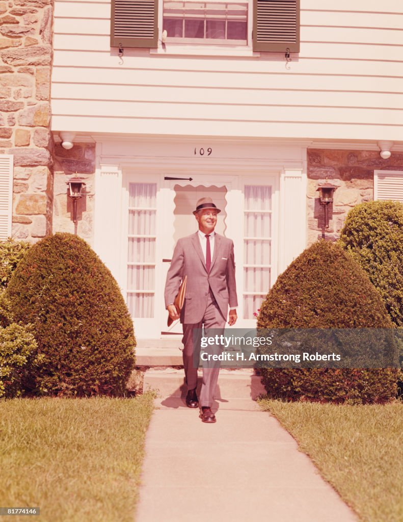 Salesman wearing hat and carrying briefcase, walking along suburban street. (Photo by H. Armstrong Roberts/Retrofile/Getty Images)