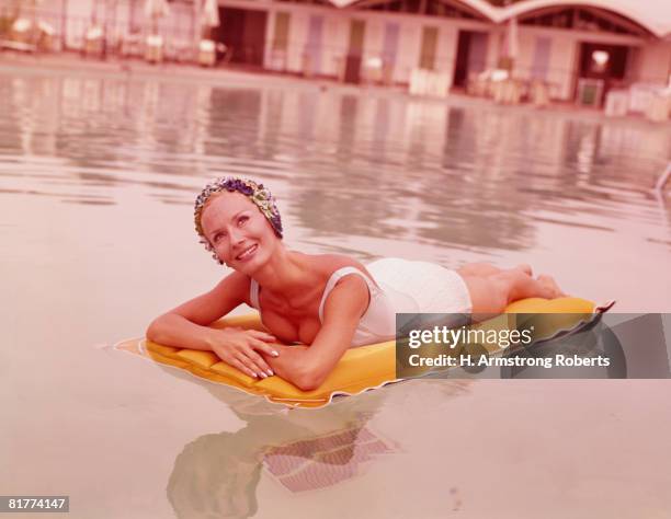 woman in swimming pool reclining on inflatable raft, wearing bathing cap, smiling. (photo by h. armstrong roberts/retrofile/getty images) - retro swimwear stock pictures, royalty-free photos & images