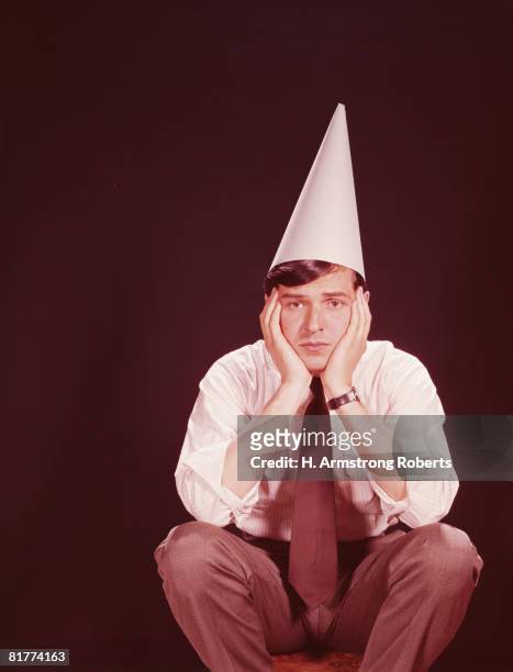 man sitting on stool, wearing dunce's hat. (photo by h. armstrong roberts/retrofile/getty images) - dunce cap stock-fotos und bilder