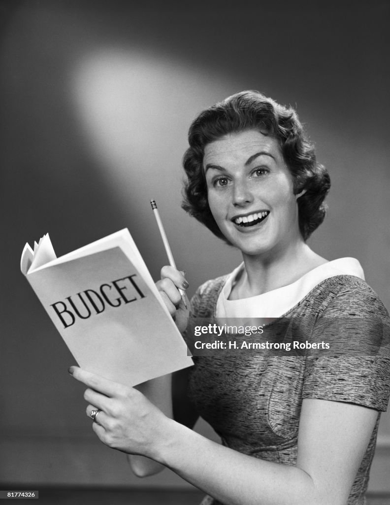 Portrait of woman smiling, holding up pencil & budget book. (Photo by H. Armstrong Roberts/Retrofile/Getty Images)