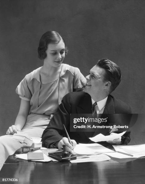 couple sitting at desk, man looking up at woman seated on arm of the chair. (photo by h. armstrong roberts/retrofile/getty images) - retrofile foto e immagini stock