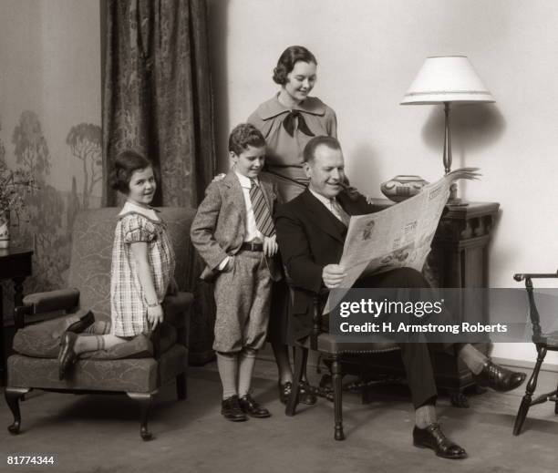 mother and children look over father's shoulder as he reads newspaper. - lee armstrong fotografías e imágenes de stock