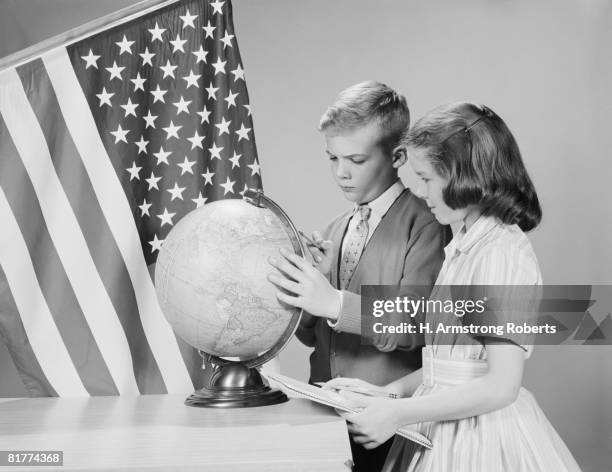 boy and girl standing at desk, looking at globe, american flag in background. (photo by h. armstrong roberts/retrofile/getty images) - retrofile foto e immagini stock