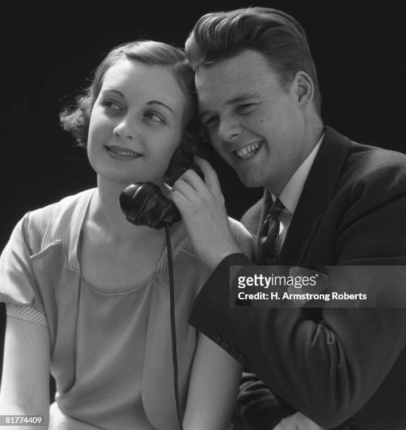 couple holding telephone receiver, both listening to conversation. (photo by h. armstrong roberts/retrofile/getty images) - retrofile foto e immagini stock