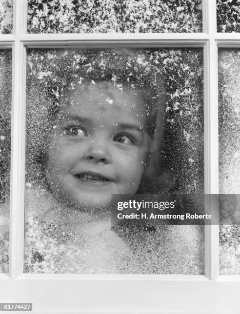 girl looking through snow-covered window. (photo by h. armstrong roberts/retrofile/getty images) - retrofile foto e immagini stock