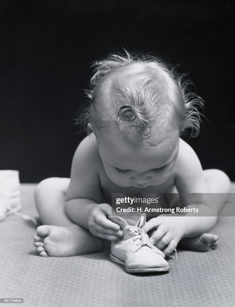 Baby leaning over playing with shoe.
