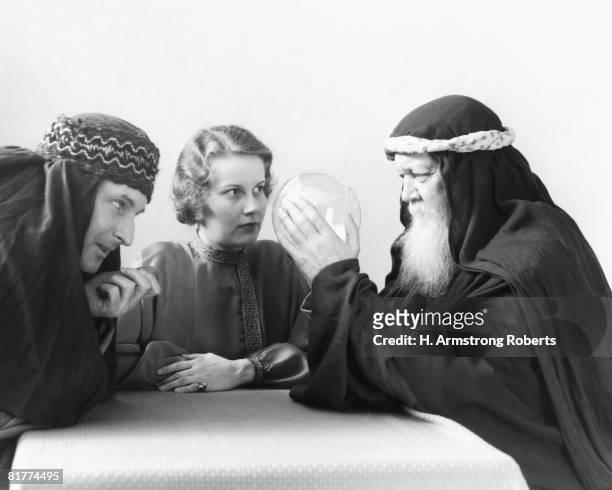 swami looking into crystal ball, with woman and man watching intently. - medium group of people foto e immagini stock
