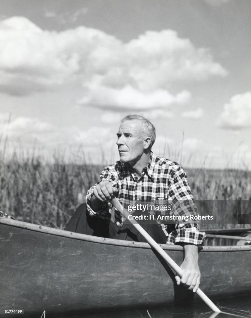 Man in plaid shirt paddling canoe on lake, Ontario Canada.