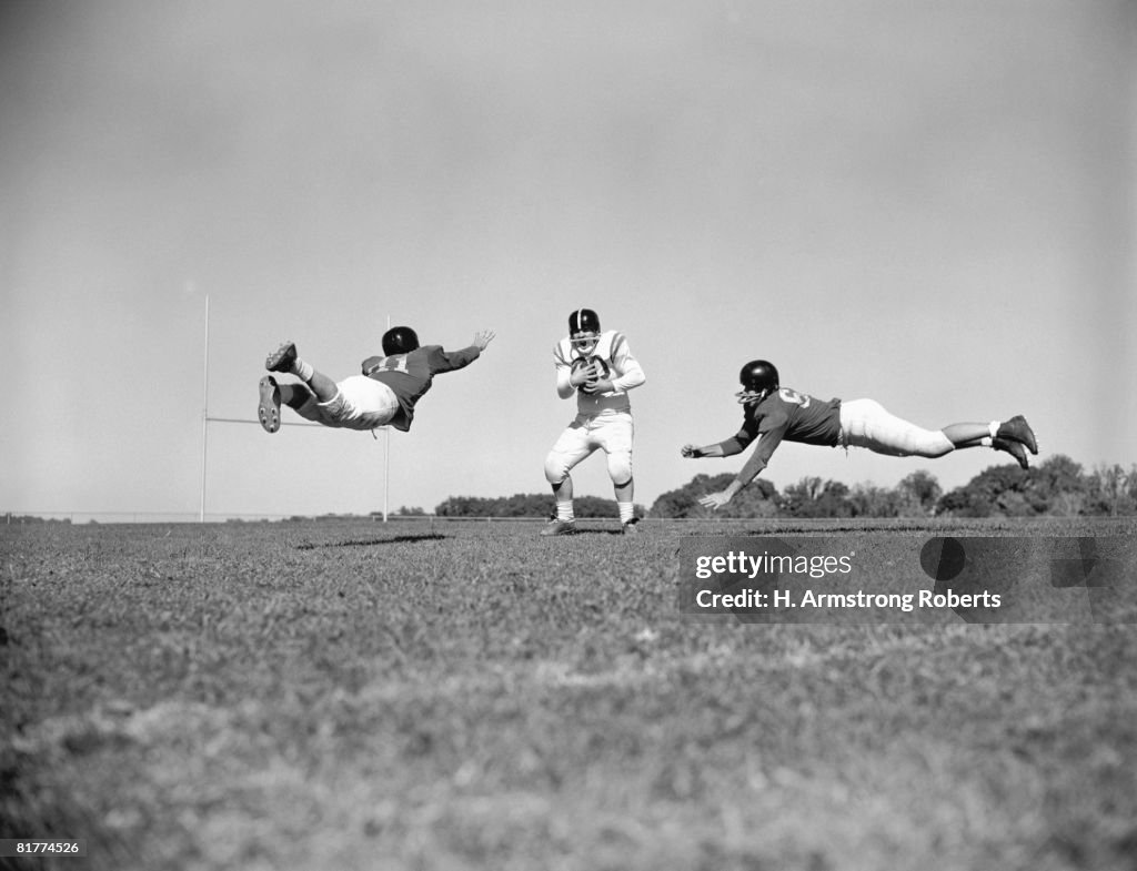 Three teenage boys playing American football, two about to tackle boy holding ball.