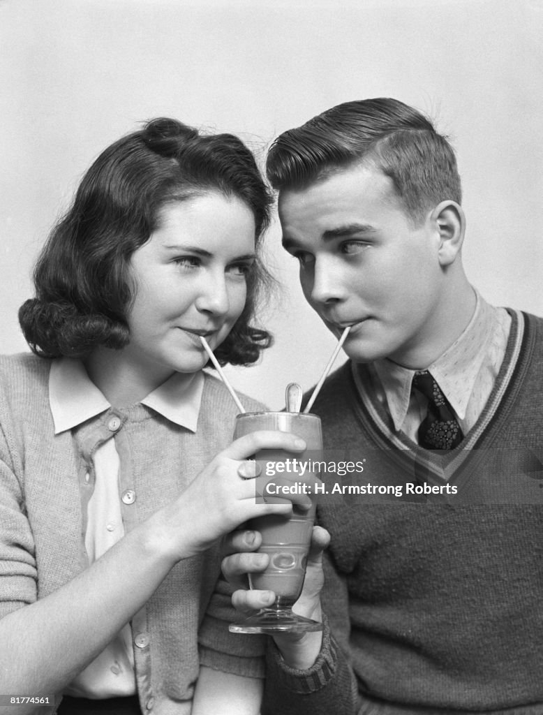 Teenage couple sipping a chocolate soda from two straws.