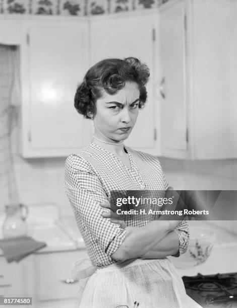 housewife in kitchen, arms folded, with serious expression. - bored housewife stock pictures, royalty-free photos & images