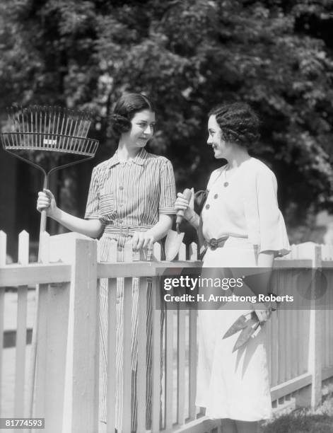 women with rake clippers and trowel chatting over picket fence. - stay at home saying stock pictures, royalty-free photos & images