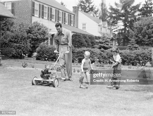 father cutting lawn with power mower, two boys using toy rake and mower. - 1950s father stock pictures, royalty-free photos & images