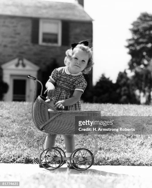 girl on sidewalk in front of house reaching into baby carriage for doll. - american girl doll stock pictures, royalty-free photos & images