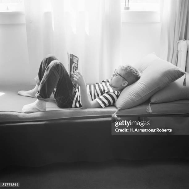 boy lying down on couch, head on cushion, reading book. - lee armstrong fotografías e imágenes de stock