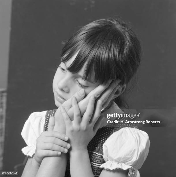 girl with sad expression resting cheek on mother's hand. - 20th century stockfoto's en -beelden