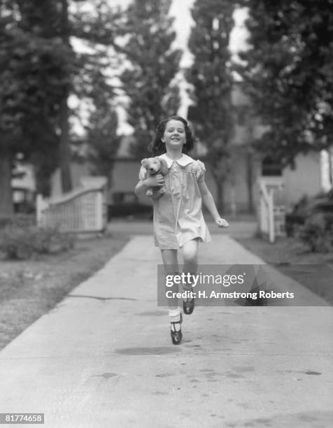 happy, carefree girl running down sidewalk, holding stuffed animal under arm. - alleen één meisje stockfoto's en -beelden